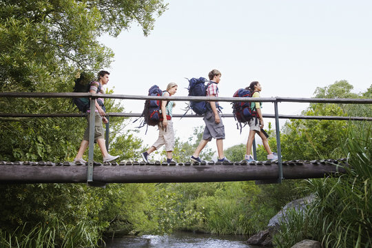 Teenage boys and girls with backpacks walking on bridge in forest