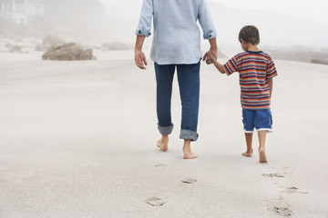 Rear view of father and son holding hands while walking on sand at beach