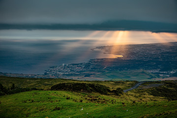 Panoramic image of Sunset city with ocean and rays of the Sun falls through dark clouds