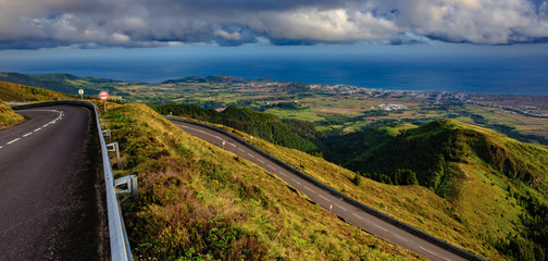 A green valley with oceanview long and winding rural path crosses the hills at the sunset