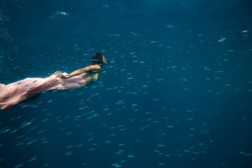 A model underwater in golden pink dress surrounded by small fish
