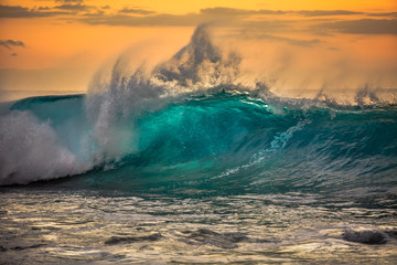 Green blue ocean splashing wave in front of orange sunset sky background - obrazy, fototapety, plakaty