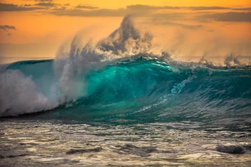 Poster Green blue ocean splashing wave in front of orange sunset sky background © willyam