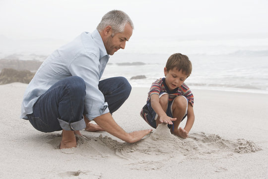 Father and son preparing sand castle together on beach