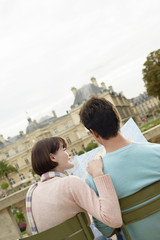Rear view of a young couple sitting on bench and looking at map