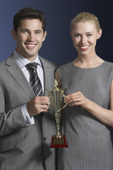 Portrait of a young businessman and woman holding a trophy against blue background