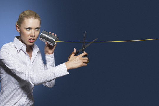 Businesswoman cutting line on tin can string phone against blue background