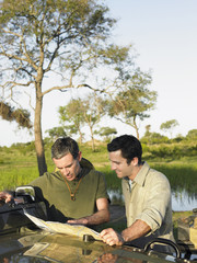 Two male friends reading map on bonnet against the lake