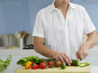 Midsection of young man cutting vegetables on wooden board in domestic kitchen