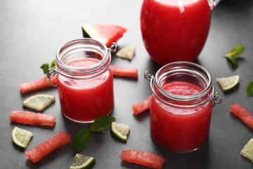 Jars with smoothie, watermelon and lime slices and mint on grey table