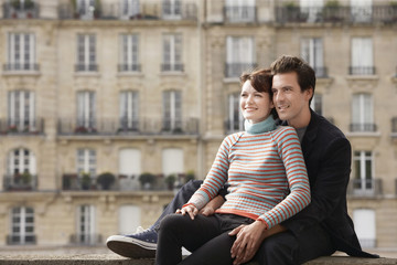 Smiling young couple sitting on bridge in front of town houses