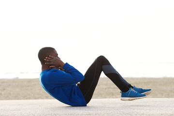 young black man exercising on the beach doing sit ups