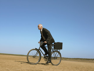 Full length of middle aged businessman riding bicycle in desert