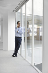 Full length of young businessman using cellphone looking through window in office