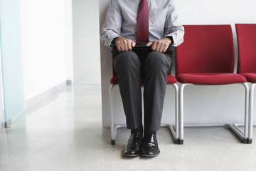 Lowsection of a male executive sitting with laptop on chair in corridor