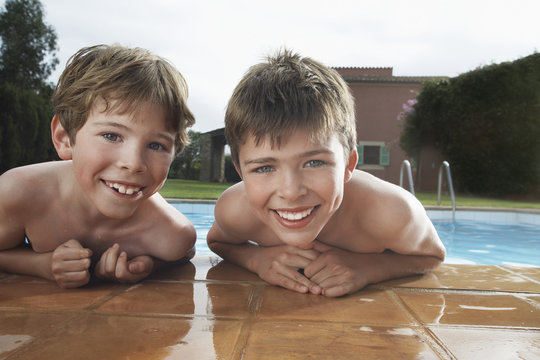 Portrait of two smiling shirtless boys leaning on pool's edge