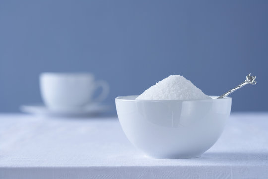Bowl of sugar on table tea cup in background