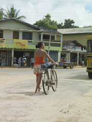 Rear view full length of a young woman on street walking with bicycle
