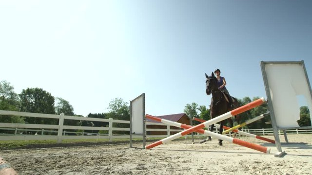 SLOW MOTION: Young girl rider jumping the oxer fence with her horse in paddock