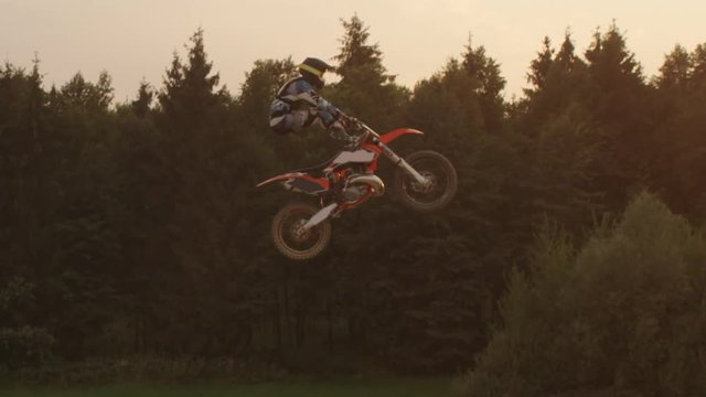 AERIAL SLOW MOTION: Extreme motocross biker jumping no hander trick at sunset