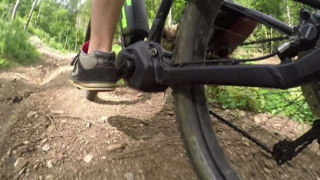 CLOSE UP: Unrecognizable biker riding electric bike uphill through the forest