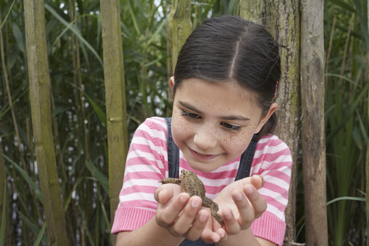 Happy young girl looking at toad in front of fence