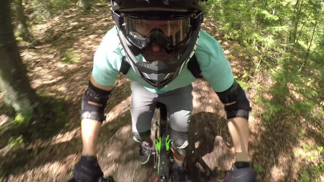 PORTRAIT CLOSE UP: Extreme biker riding downhill trail in dense green forest