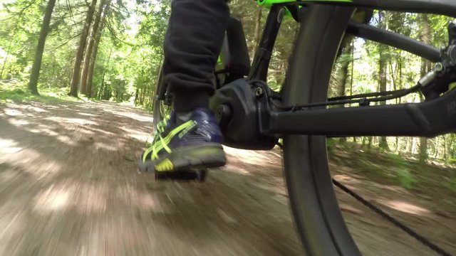 CLOSE UP: Biker riding electric bicycle fast on gravel dirt road in sunny forest