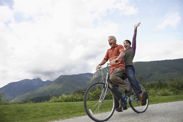 Low angle view of a cheerful middle aged couple riding bicycle on country road