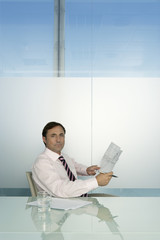 Portrait of confident businessman holding document while sitting at desk in office