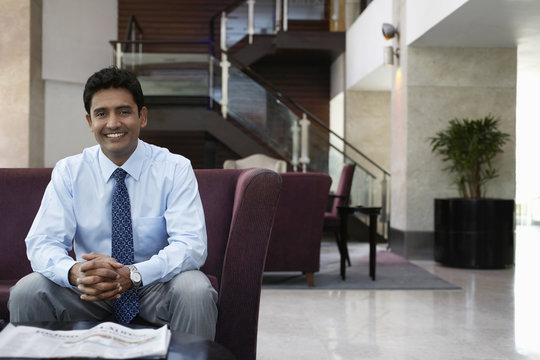 Portrait of happy young businessman sitting on sofa in hotel lobby