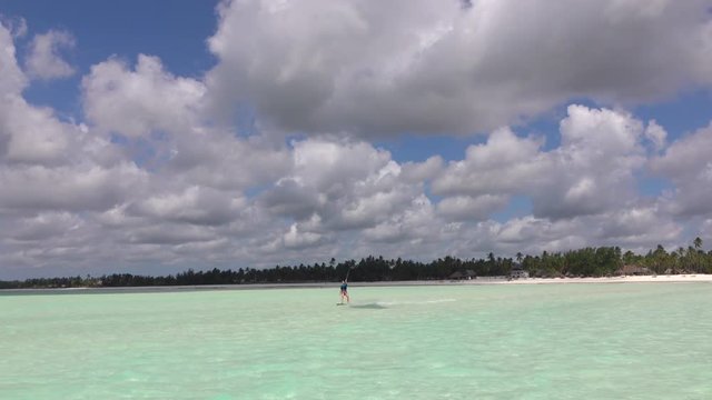 Woman kiteboarder kiting in perfect blue lagoon in front of exotic sandy beach