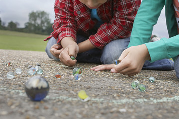Low section of brother and sister playing marbles on playground - Powered by Adobe
