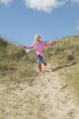 Naklejka na ściany i meble Full length of excited young girl running down sand dunes