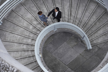High angle view of businessman and businesswoman shaking hands on spiral staircase
