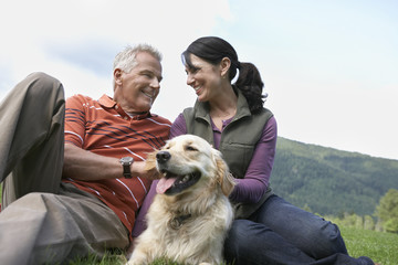 Happy middle aged couple and golden retriever relaxing on grass