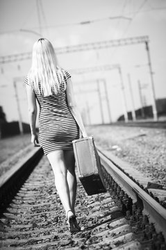 beautiful girl with a suitcase walking on railroad tracks
