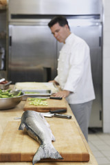 Side view of a cropped male chef in kitchen with focus on salmon in foreground
