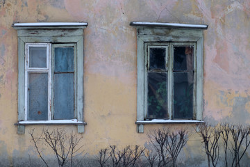 Ветхие окна с деревянными рамами старого жилого дома с потрескавшейся штукатуркой 