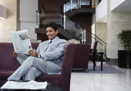 Happy young businessman reading newspaper in hotel lobby