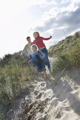 Full length of parents and daughter running through sand dunes on beach