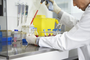 Closeup of a cropped male scientist filling test tube with hitech pipette in laboratory