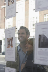 Fototapeta premium Closeup of a cheerful young couple looking through window at estate agents