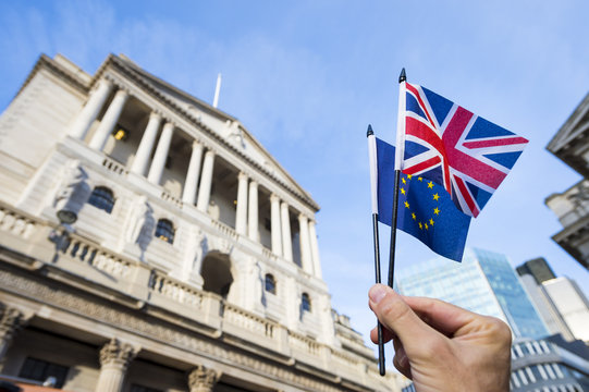 Hand holding European Union and British Union Jack flags in front of the Bank of England as symbols of the financial repercussions of the Brexit EU referendum