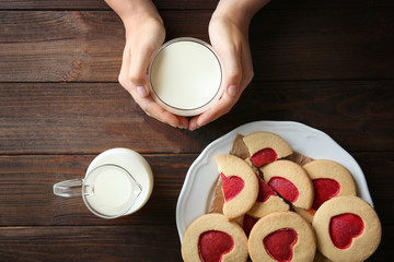 Female hands with milk and cookies on wooden table, top view