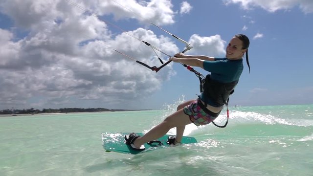 SLOW MOTION: Happy smiling surfer girl has fun kitesurfing in blue ocean