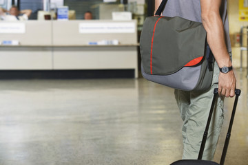 Closeup side view midsection of a male traveler with bags at the airport