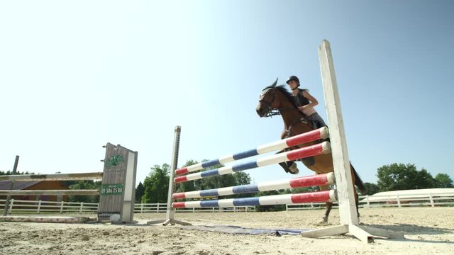 SLOW MOTION: Young competitive rider girl training fence jumping on sandy manege