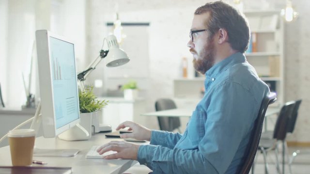 Close-up of a Young Bearded Man Working on Personal Computer in His Light and Modern Office.  Shot on RED Cinema Camera in 4K (UHD).