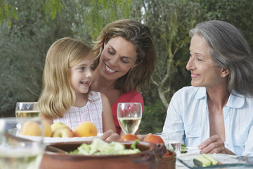 Grandmother, mother and daughter sitting at table in garden
